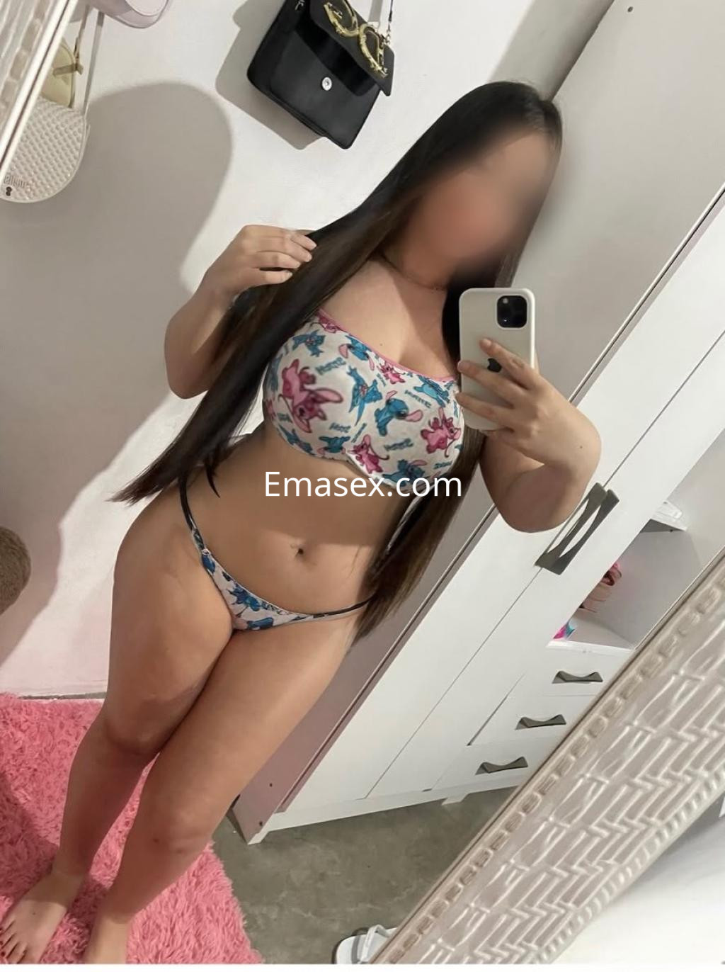 Puta en Bilbao con cabello largo y lacio, vestida con un conjunto de bikini floral frente a un espejo.