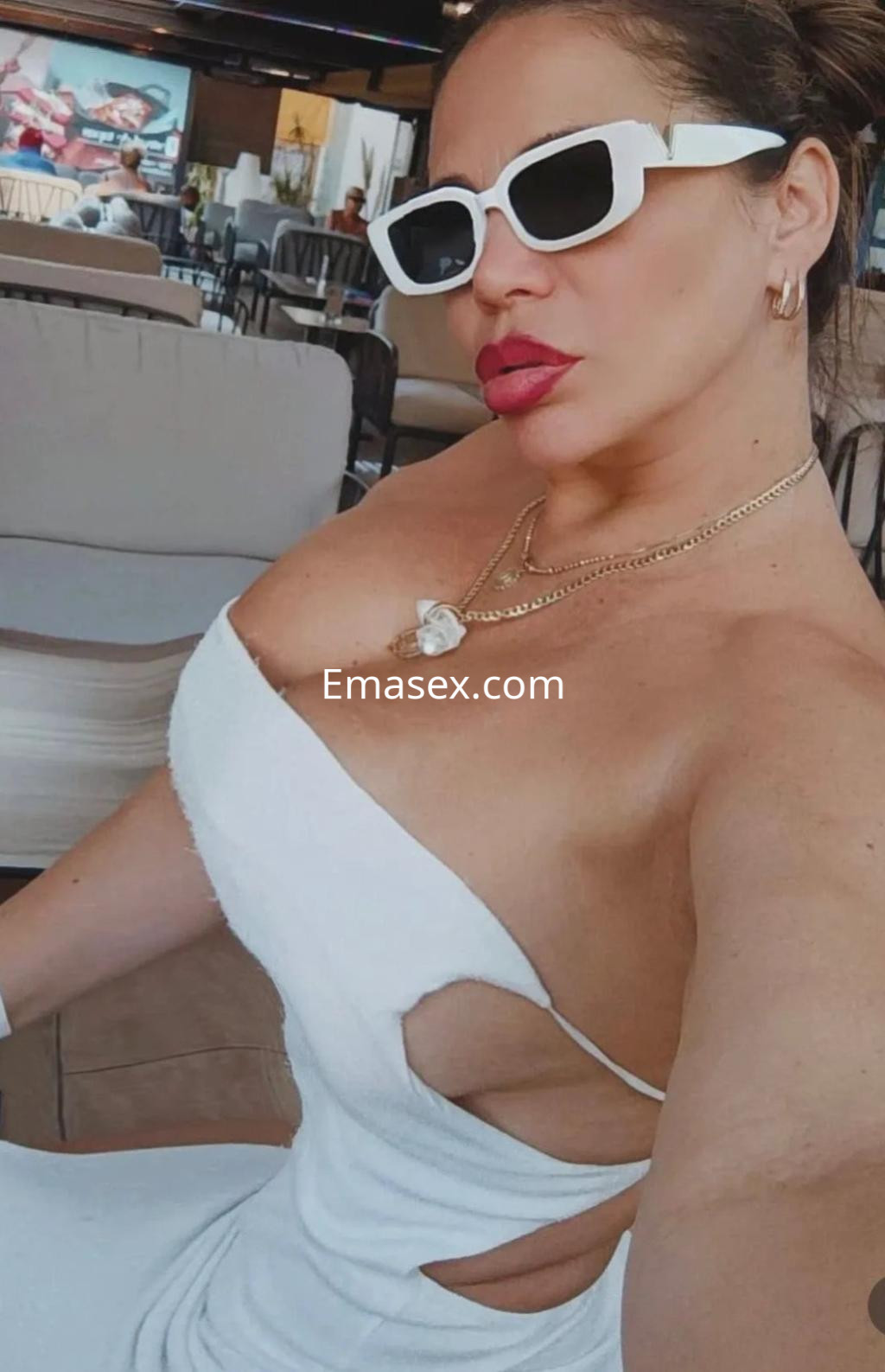 Puta en Málaga lleva un vestido blanco ajustado y gafas de sol, posando con una expresión coqueta.