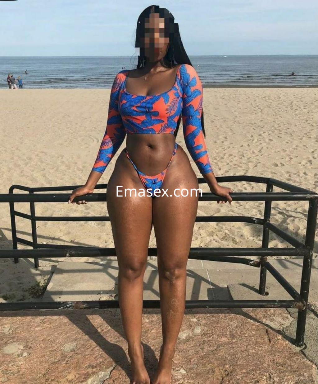 Puta con traje de baño colorido en la playa de Albacete, mostrando una pose segura y sonriente.
