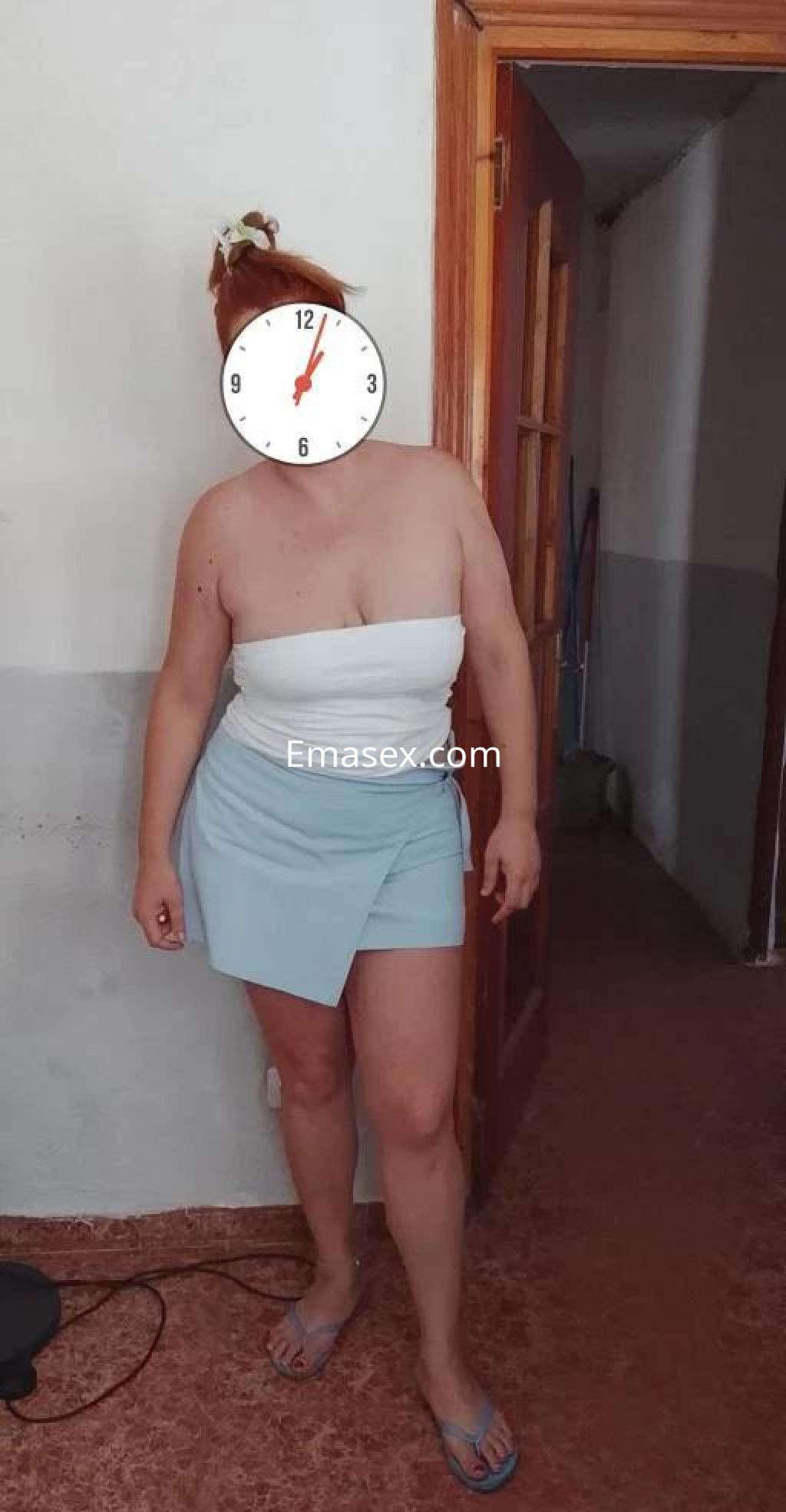 Escort en Almería con blusa blanca y falda corta azul, posando en un interior con puertas de madera.