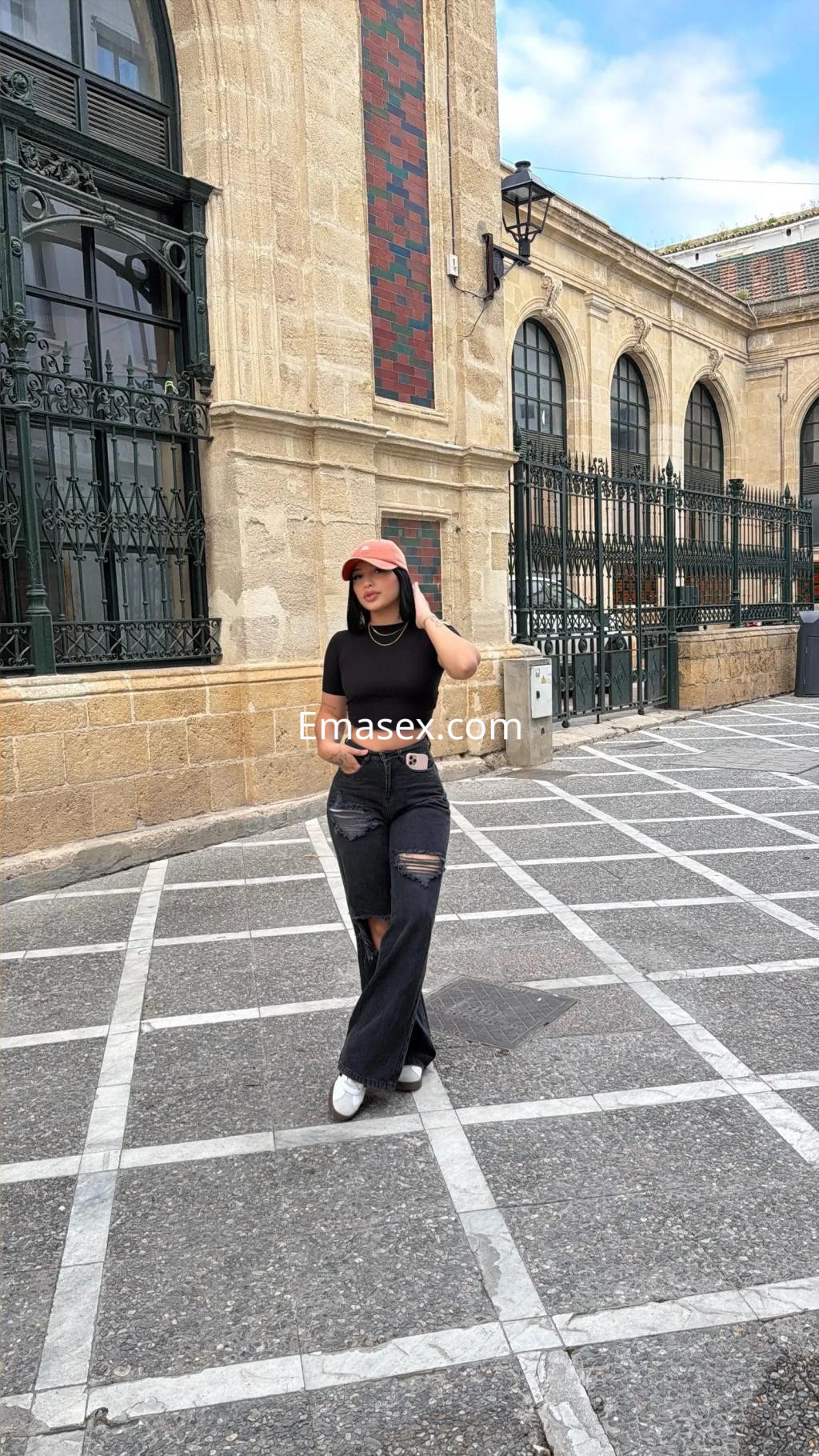La puta posa en una calle de Cádiz, luciendo una camiseta negra y pantalones rasgados, con una gorra.