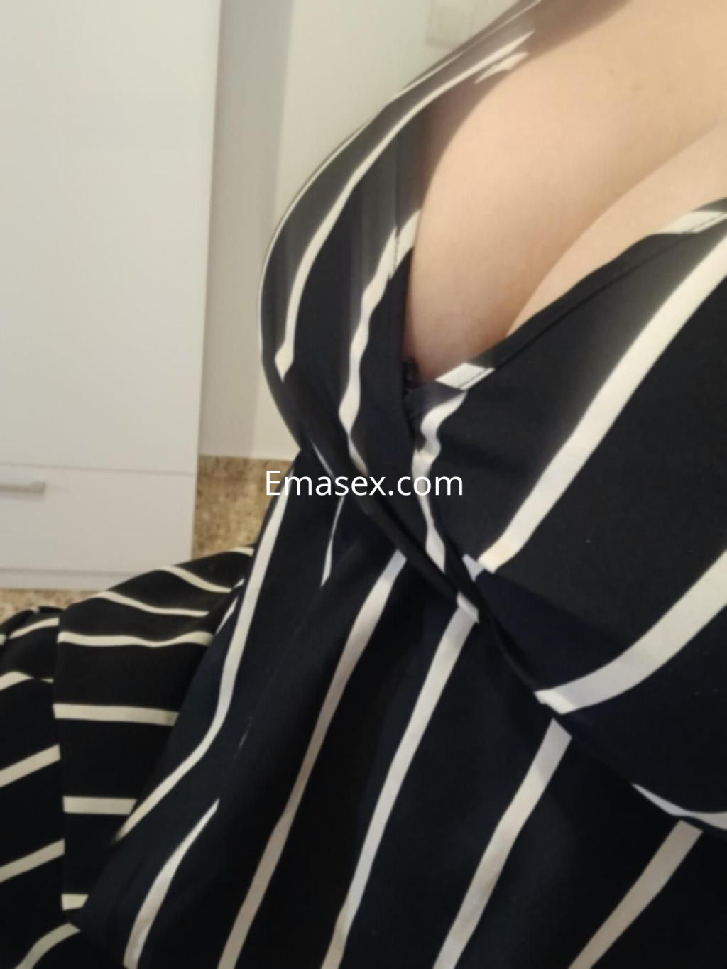 La puta en Castellón luce un vestido negro con rayas blancas, destacando su escote y figura.