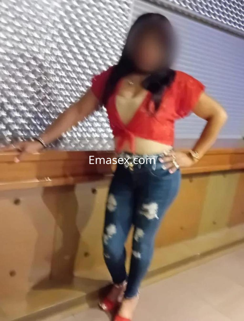 Escort en Lleida, vistiendo una blusa roja corta y jeans ajustados, posando con una mano en la cadera.