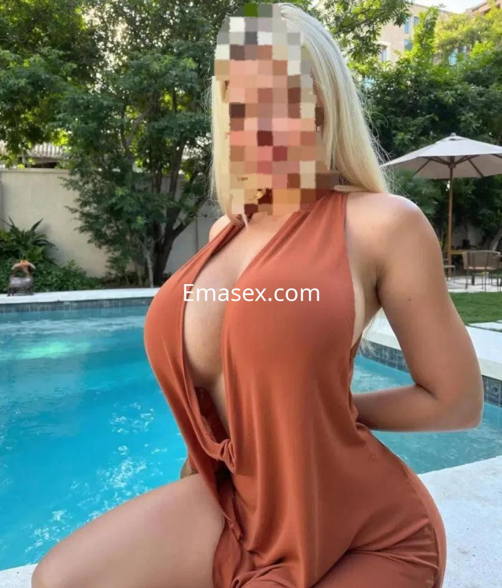 Puta en Lleida, posando junto a una piscina, con un vestido marrón que resalta su figura y cabello rubio.