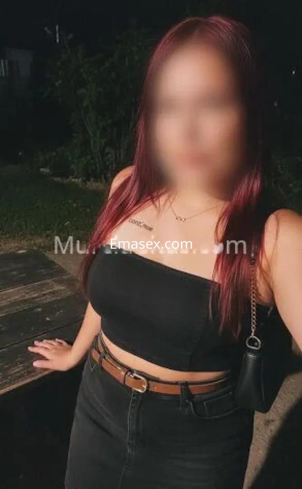 Escort en Murcia con cabello largo y rojo, vistiendo cropped top negro y falda ajustada, posando al aire libre.
