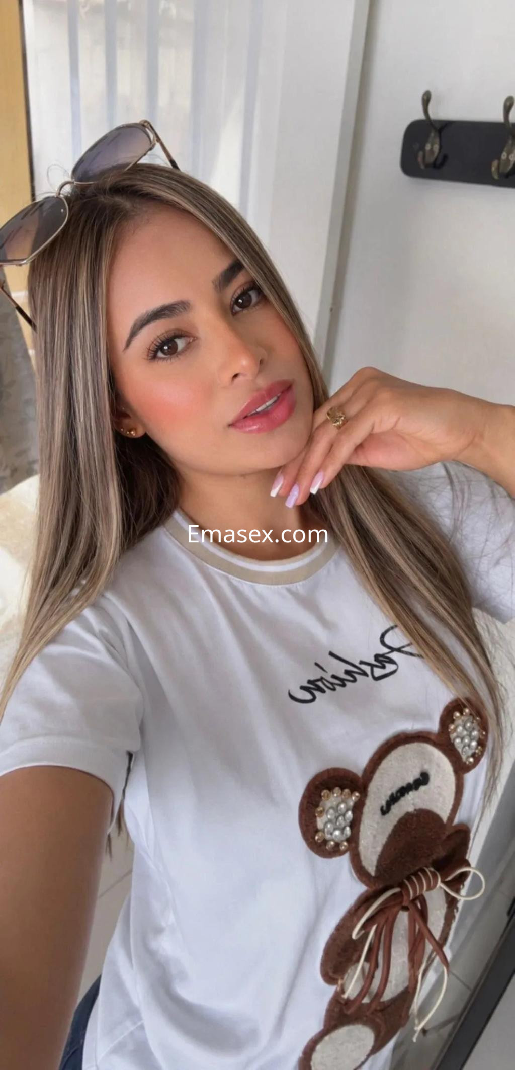 Escort con cabello largo y lacio, vistiendo una camiseta blanca con estampado de oso, en un ambiente luminoso en Valencia.