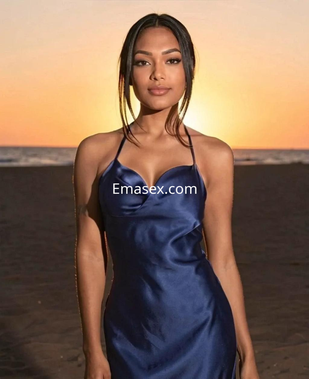 Escort en Valencia luciendo un vestido azul oscuro, con el cabello suelto y un fondo de atardecer en la playa.