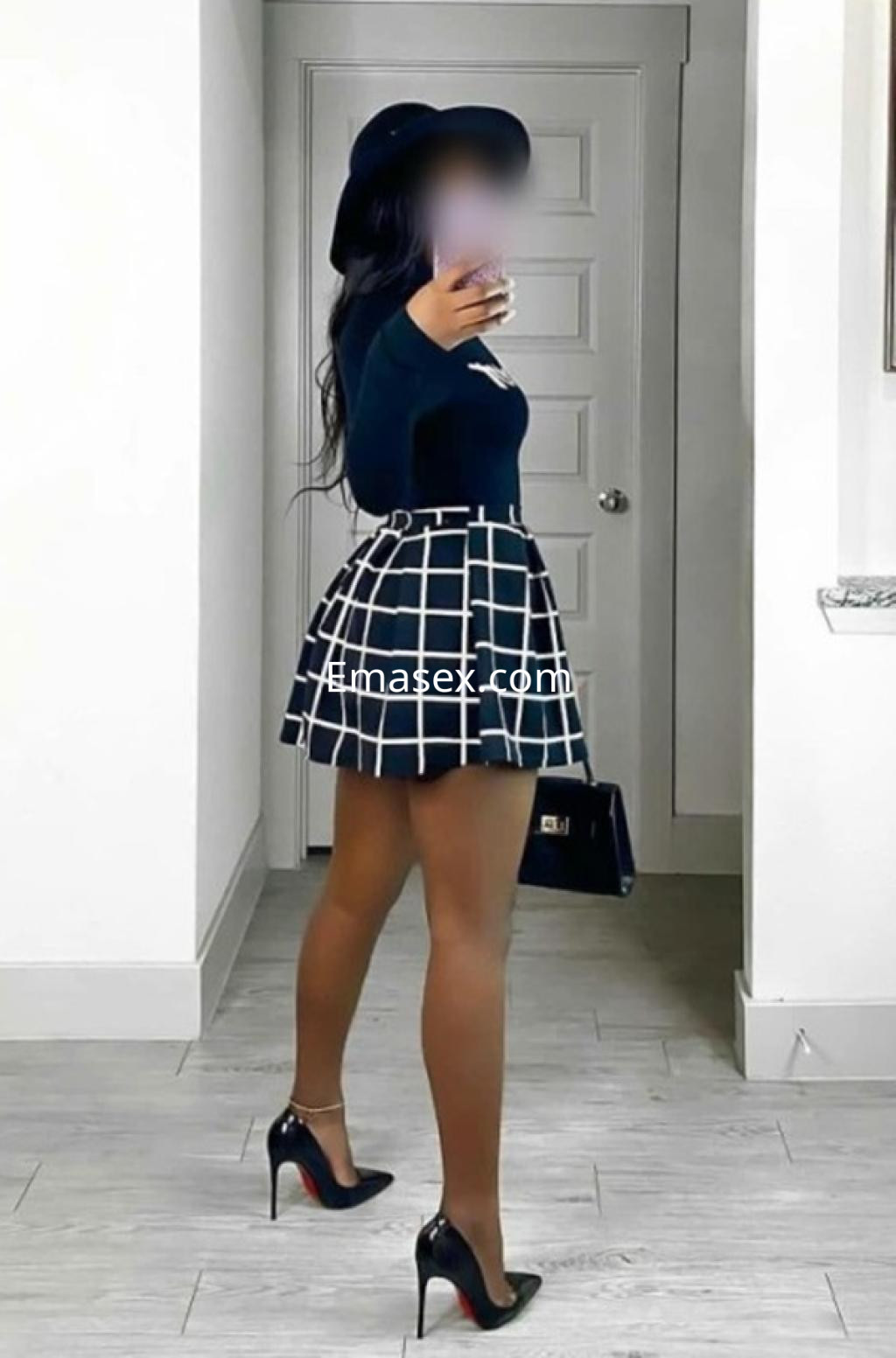Puta en Santander, vistiendo una blusa negra y una minifalda a cuadros, con tacones altos y un sombrero.