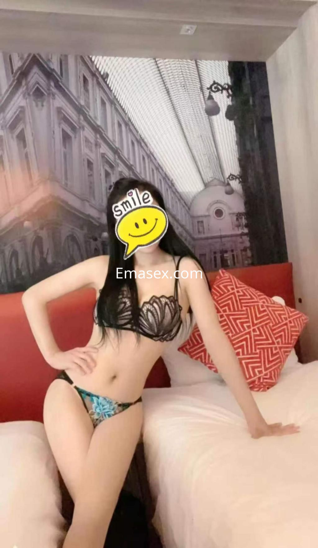 La puta en Almería posa con lencería negra y azul, sentada sobre una cama en un ambiente elegante.