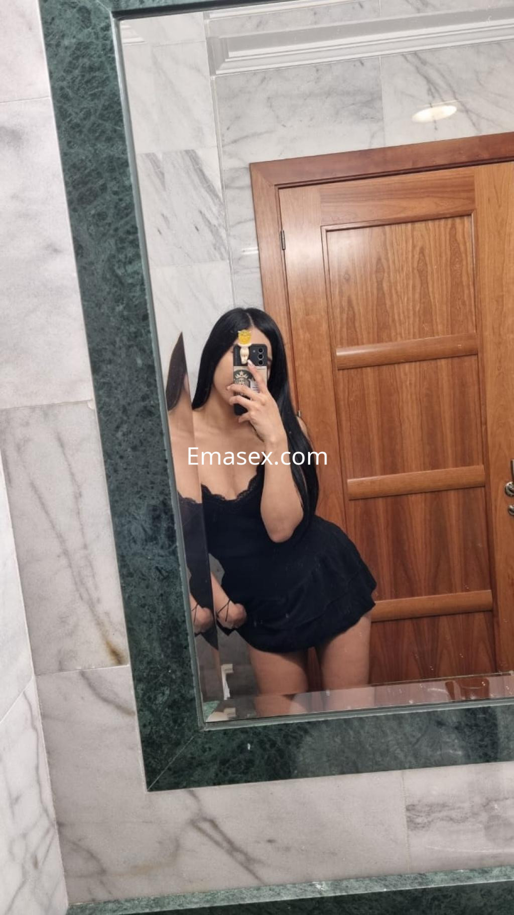 Escort en Tarragona con cabello largo y oscuro, vistiendo un top negro, posando frente a un espejo.