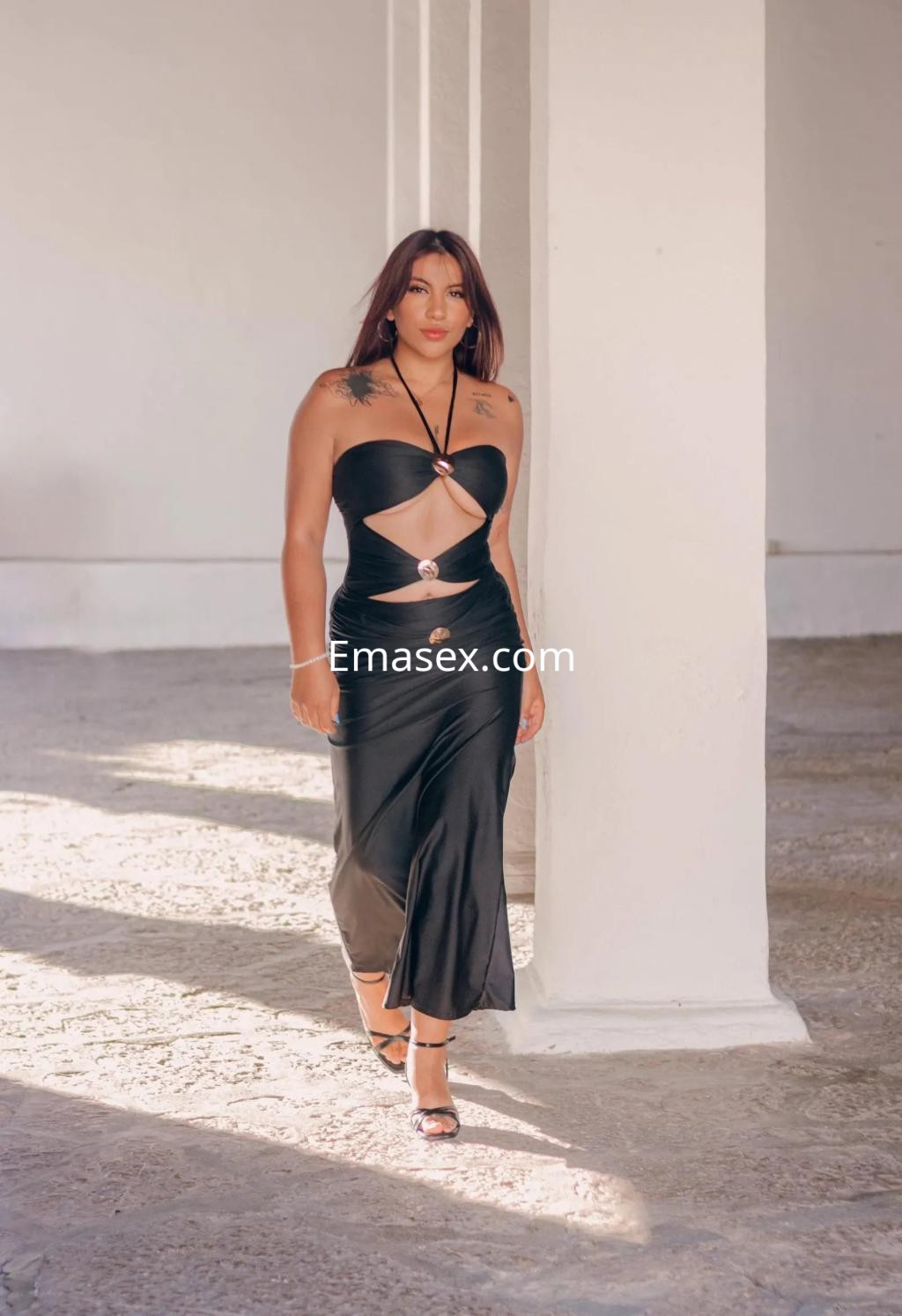 Escort en Palma de Mallorca con vestido negro ajustado y detalles en la cintura, caminando con confianza.
