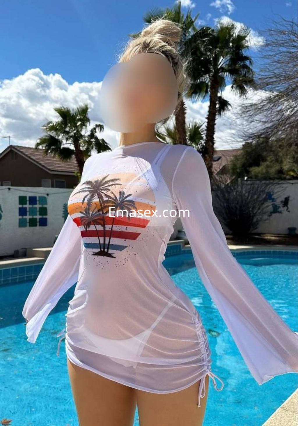 Escort en Castellón, con un vestido blanco semitransparente y un diseño colorido, posando junto a una piscina.