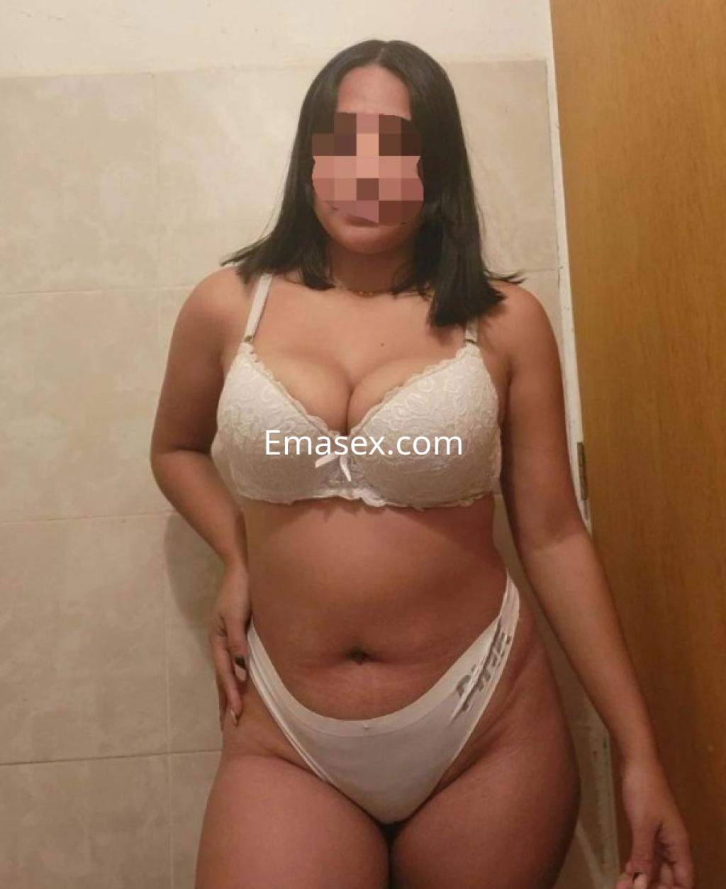 Escort en Coruña posando con un sujetador blanco y tanga, en un entorno interior con paredes de azulejos.