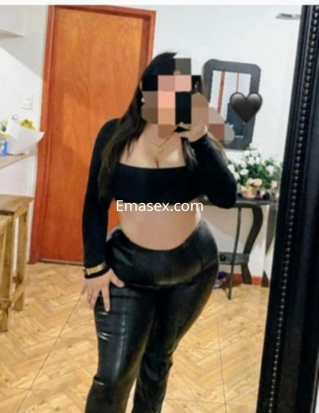 Puta con blusa negra ajustada y pantalones de cuero, posando en un interior con decoración sencilla en Oviedo.