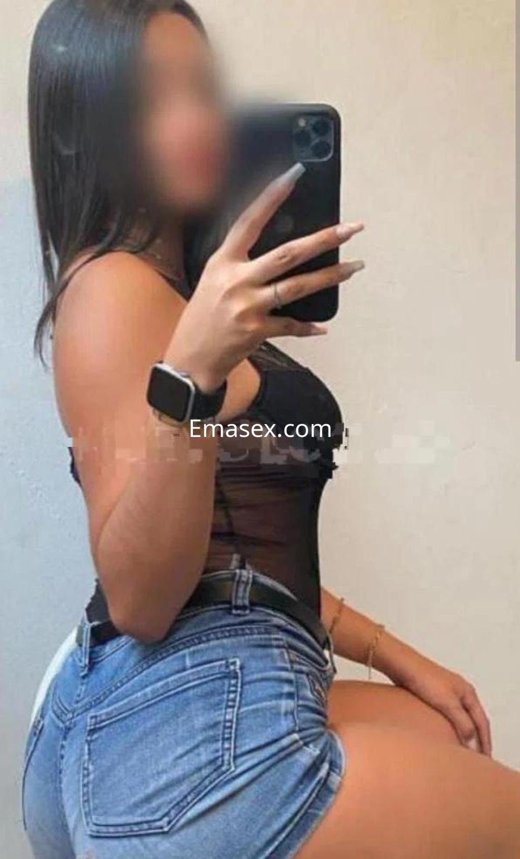 Escort en Sevilla posando con una blusa negra transparente y shorts de mezclilla, mostrando su figura.