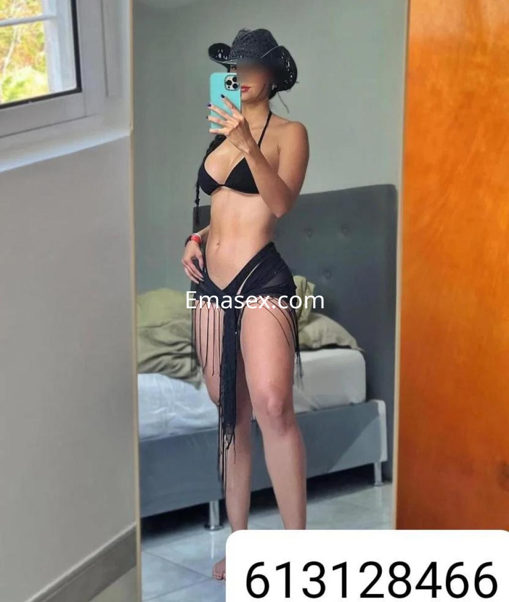 Escort en Sevilla mostrando su figura en un espejo, viste bikini negro y una falda de tiras.