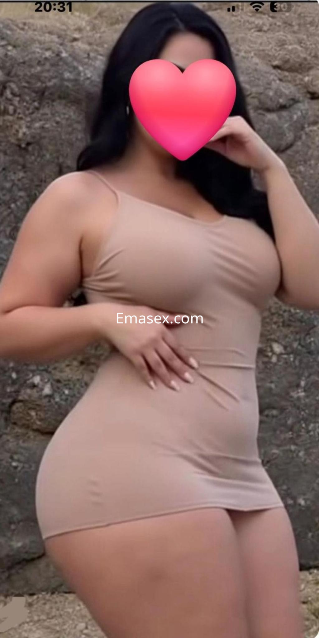 Escort en Pamplona con vestido entallado color nude, posando de perfil frente a una pared de piedra.