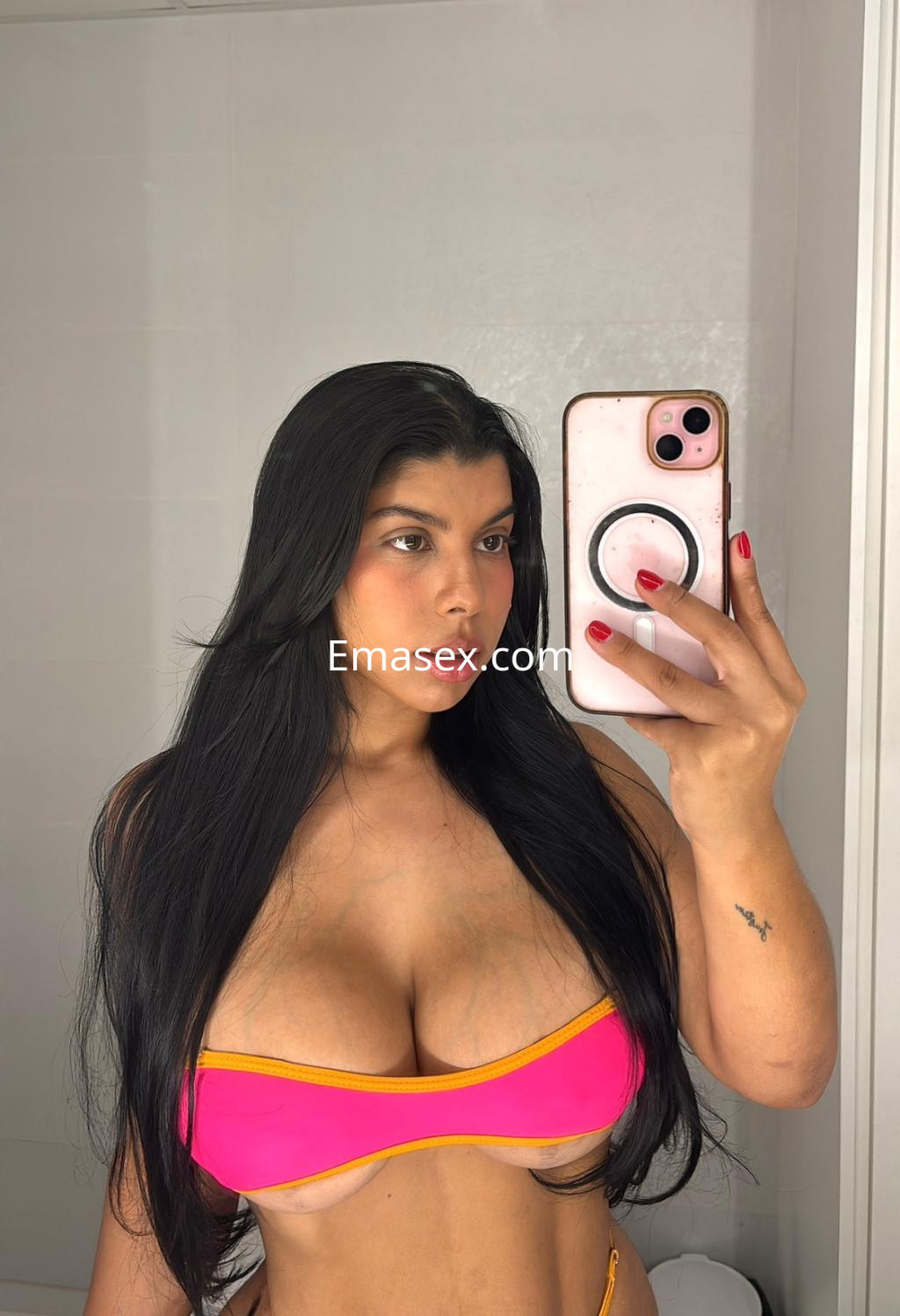 Escort en Málaga, posando frente al espejo con un bikini rosa y detalles amarillos, mostrando su figura.