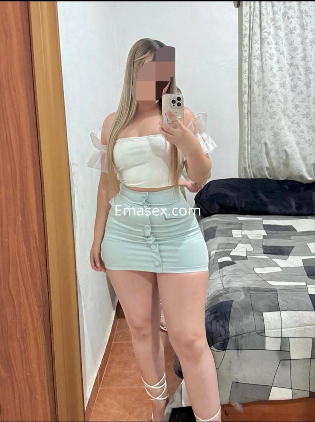 Escort en Málaga posando frente a un espejo, con blusa blanca de tirantes y falda corta de color menta.