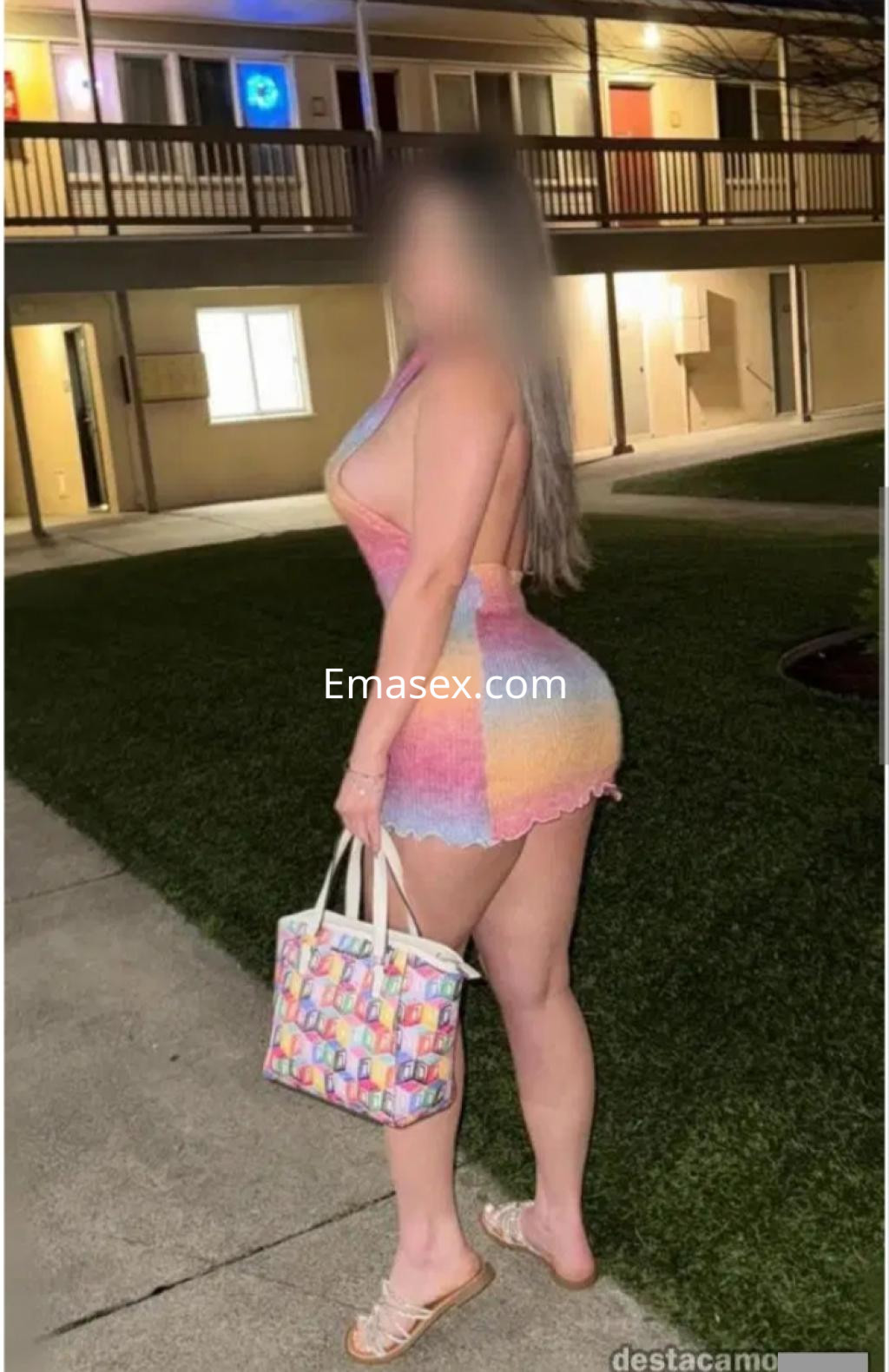 Escort en Málaga con un vestido ajustado y colorido, sosteniendo un bolso mientras posa en un entorno exterior.
