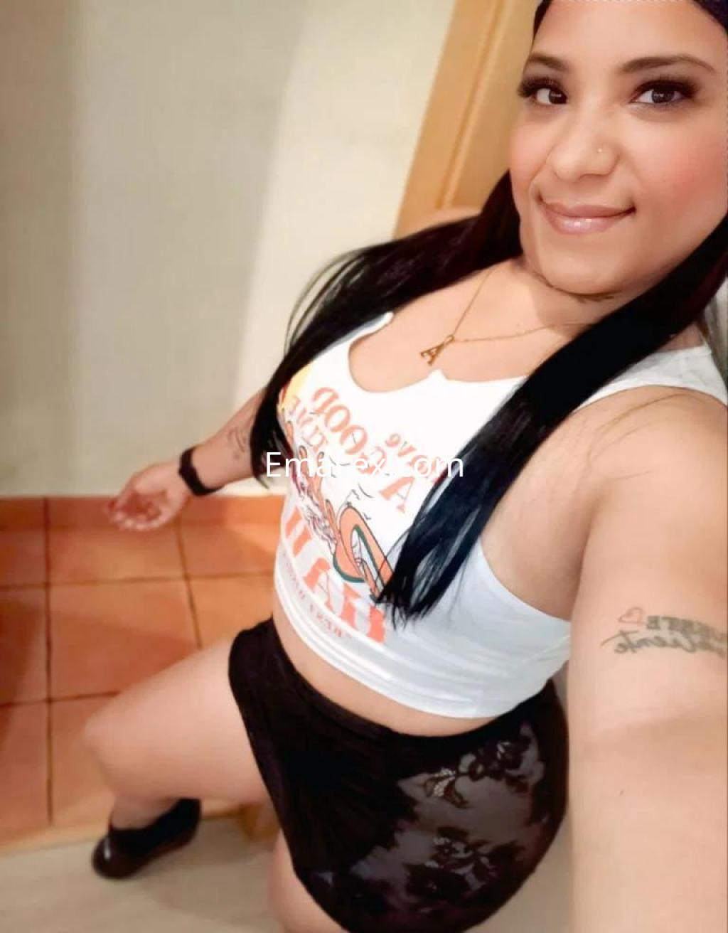 Escort en Girona con cabello largo y lacio, viste una camiseta blanca y una falda corta negra, posando sonriente.