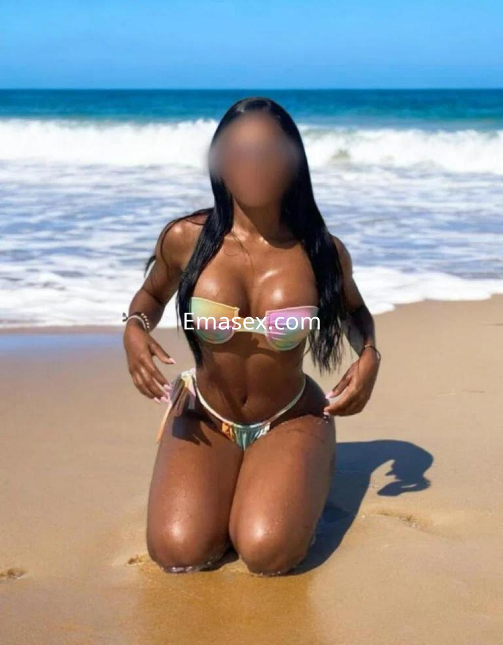 Escort de Lugo en la playa, de rodillas sobre la arena, luciendo un bikini colorido y cabello largo.