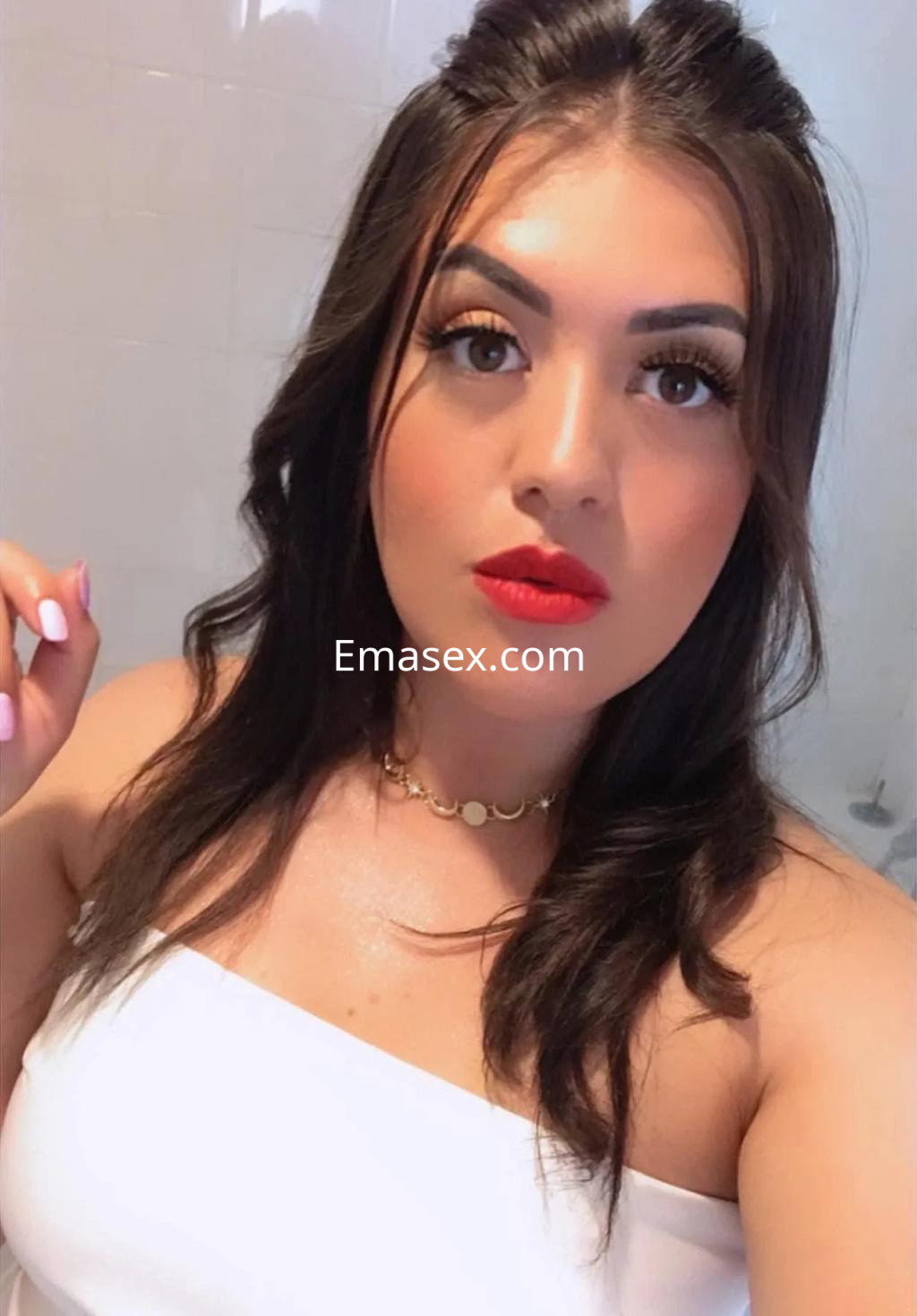 Puta en Oviedo con cabello oscuro, maquillaje destacado y blusa blanca, posando con una mirada cautivadora.