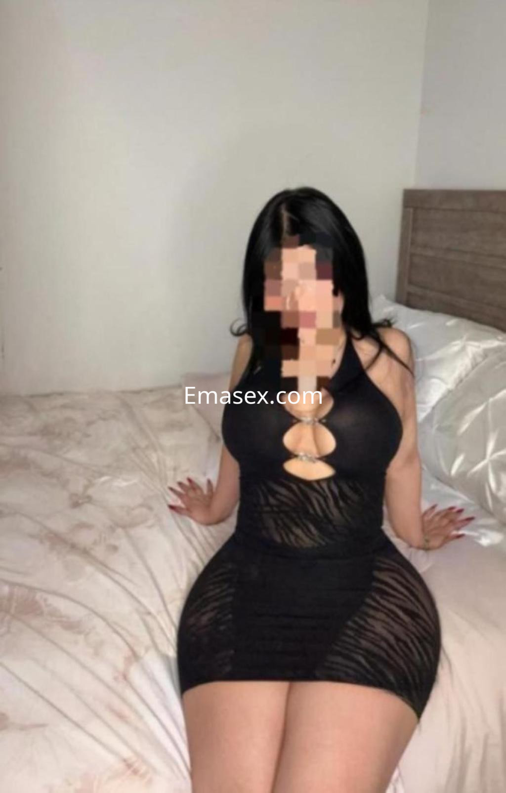 Escort en Vigo luciendo un vestido negro ajustado, sentada en una cama con sábanas claras.