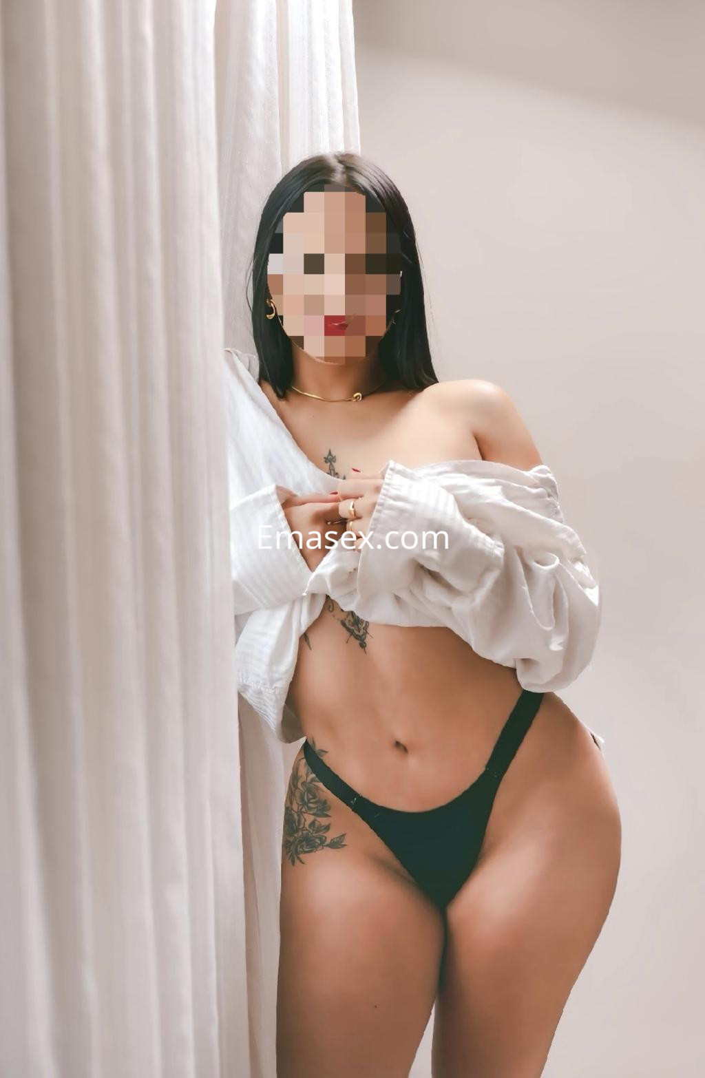 Escort en Madrid con cabello corto y lacio, vistiendo una camisa blanca abierta y una tanga negra, posando de lado.