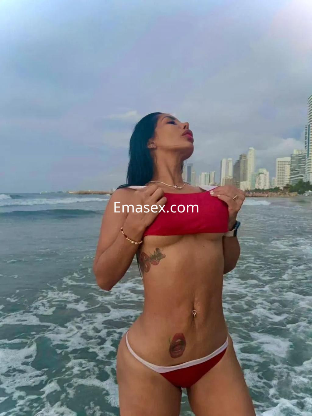 Escort en Palma de Mallorca luciendo un bikini rojo mientras posa en la orilla del mar al atardecer.