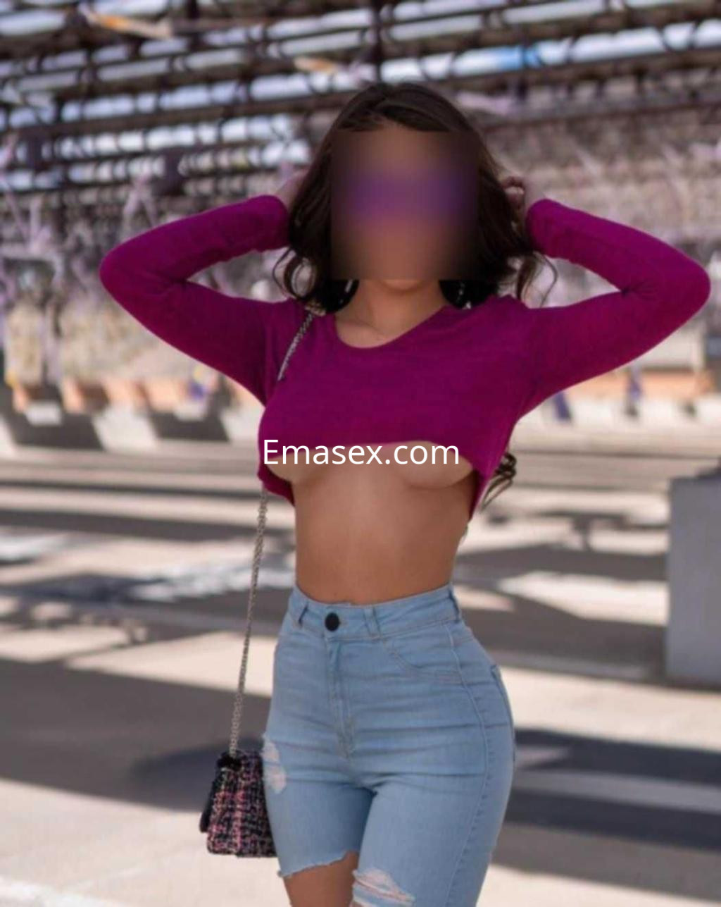 La puta en Córdoba lleva un top rosa y shorts ajustados, posando con las manos en la cabeza.