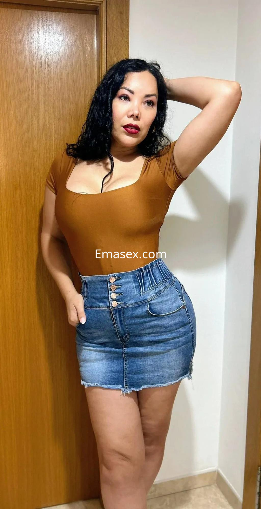 Escort en Murcia con cabello largo y oscuro, luciendo una blusa marrón y una falda de mezclilla ajustada.