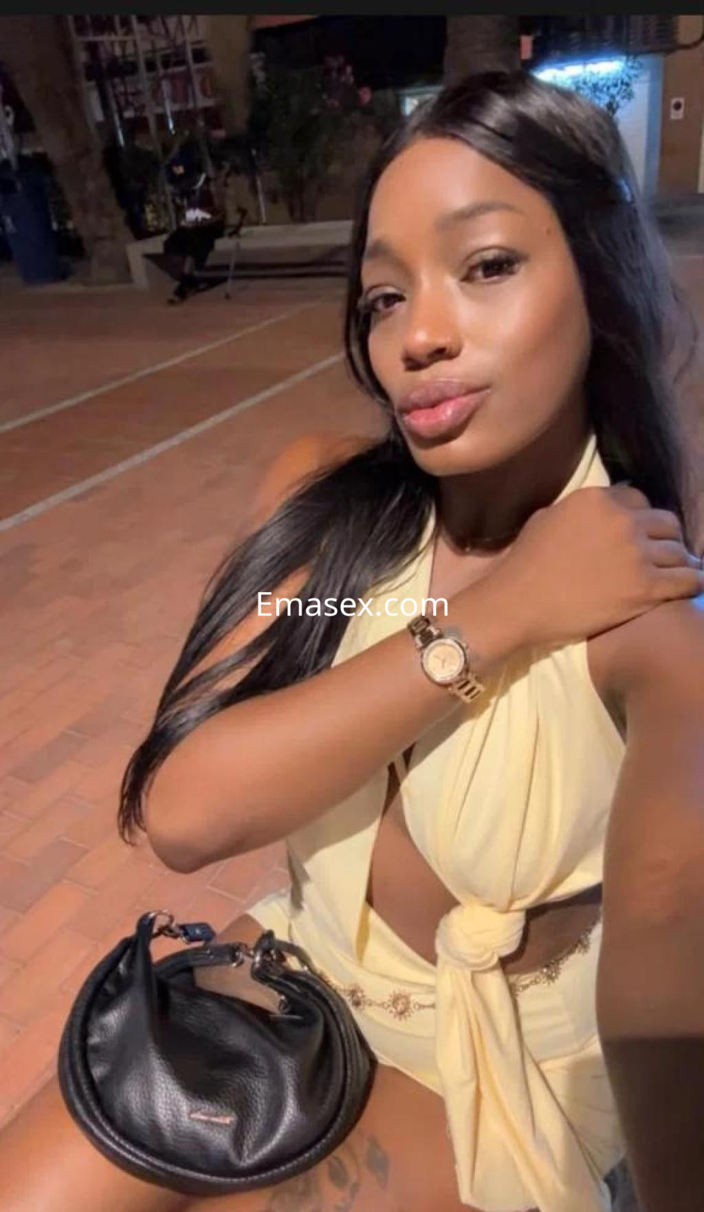 Escort en Oviedo, luciendo un vestido amarillo con un escote pronunciado y una cartera negra mientras posa al aire libre.