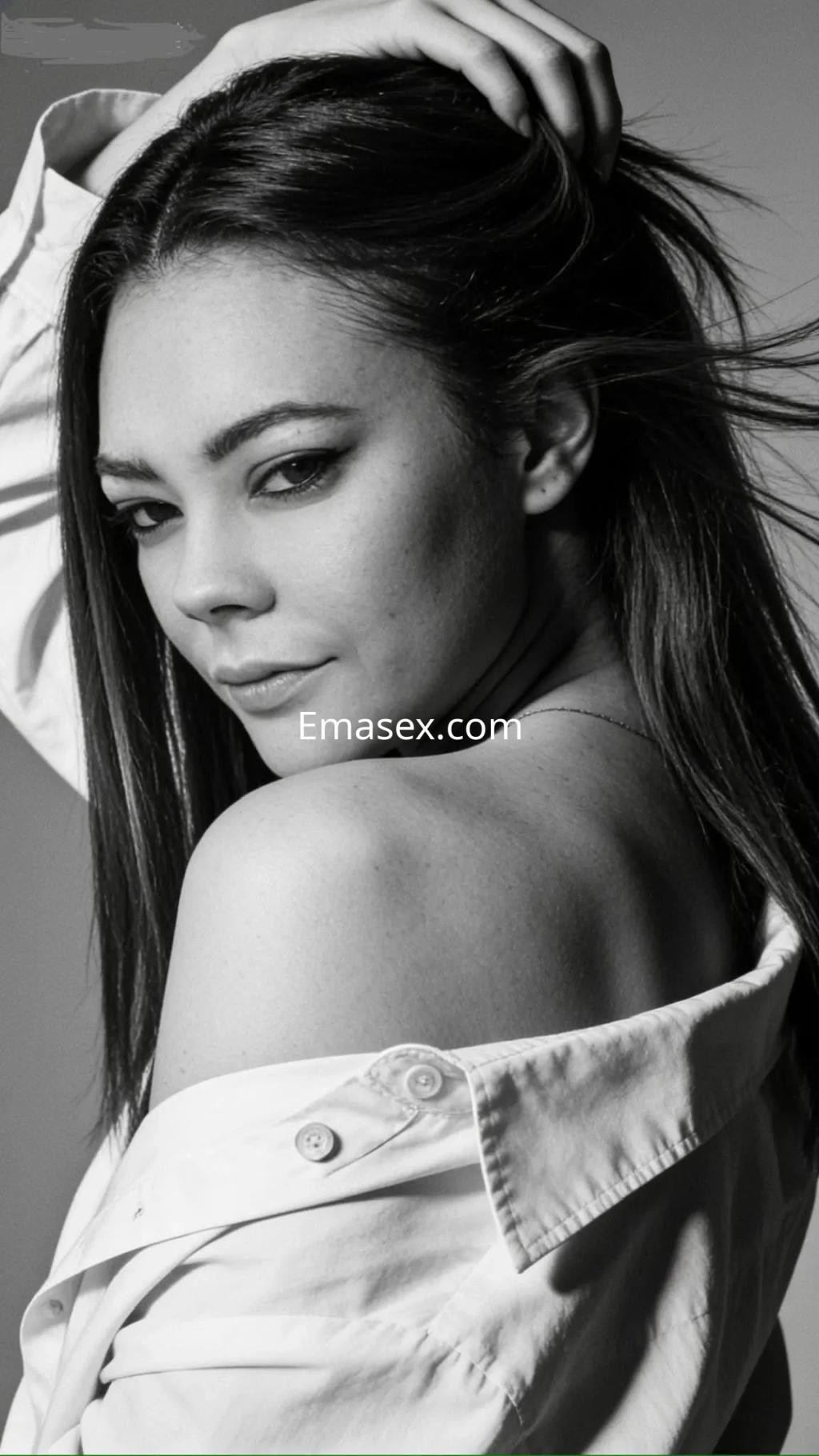 Escort en Valencia con cabello largo y lacio, posando de perfil con una camisa blanca y mirada seductora.