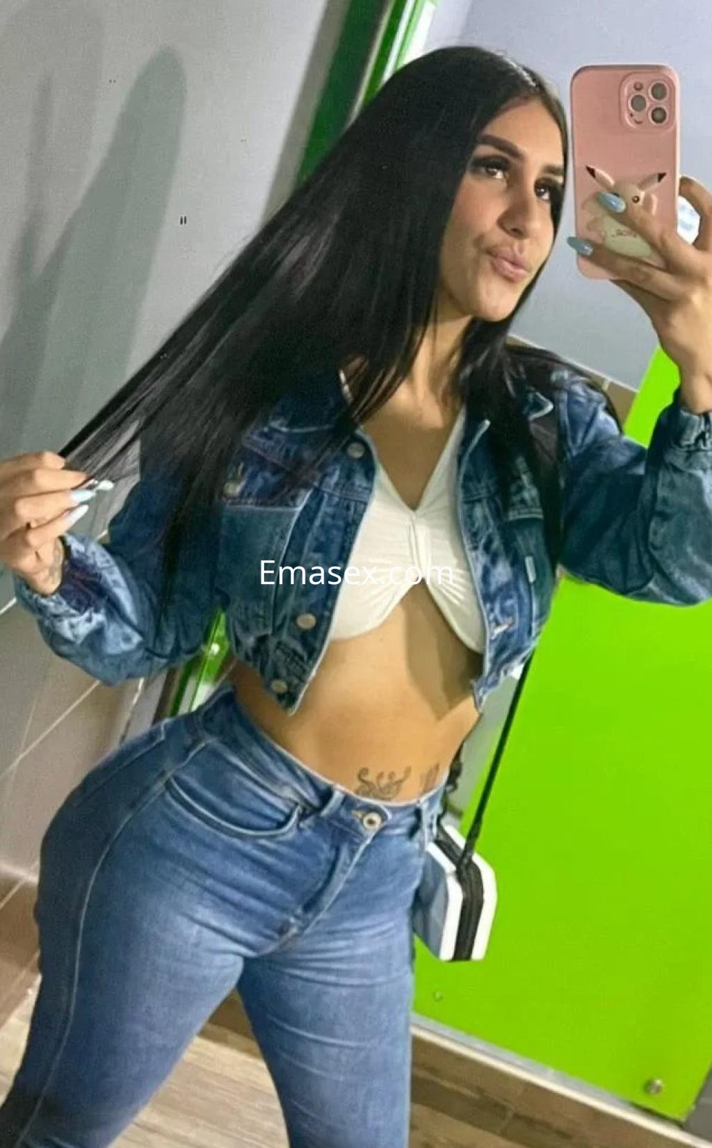 Escort en Málaga posando frente al espejo, viste un top blanco y chaqueta de mezclilla, con pantalones ajustados.