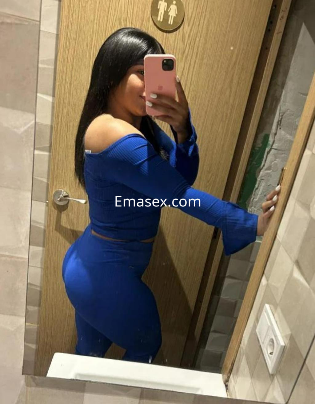 Puta posando en un espejo, viste un conjunto azul ajustado que resalta su figura, en un baño de Barcelona.