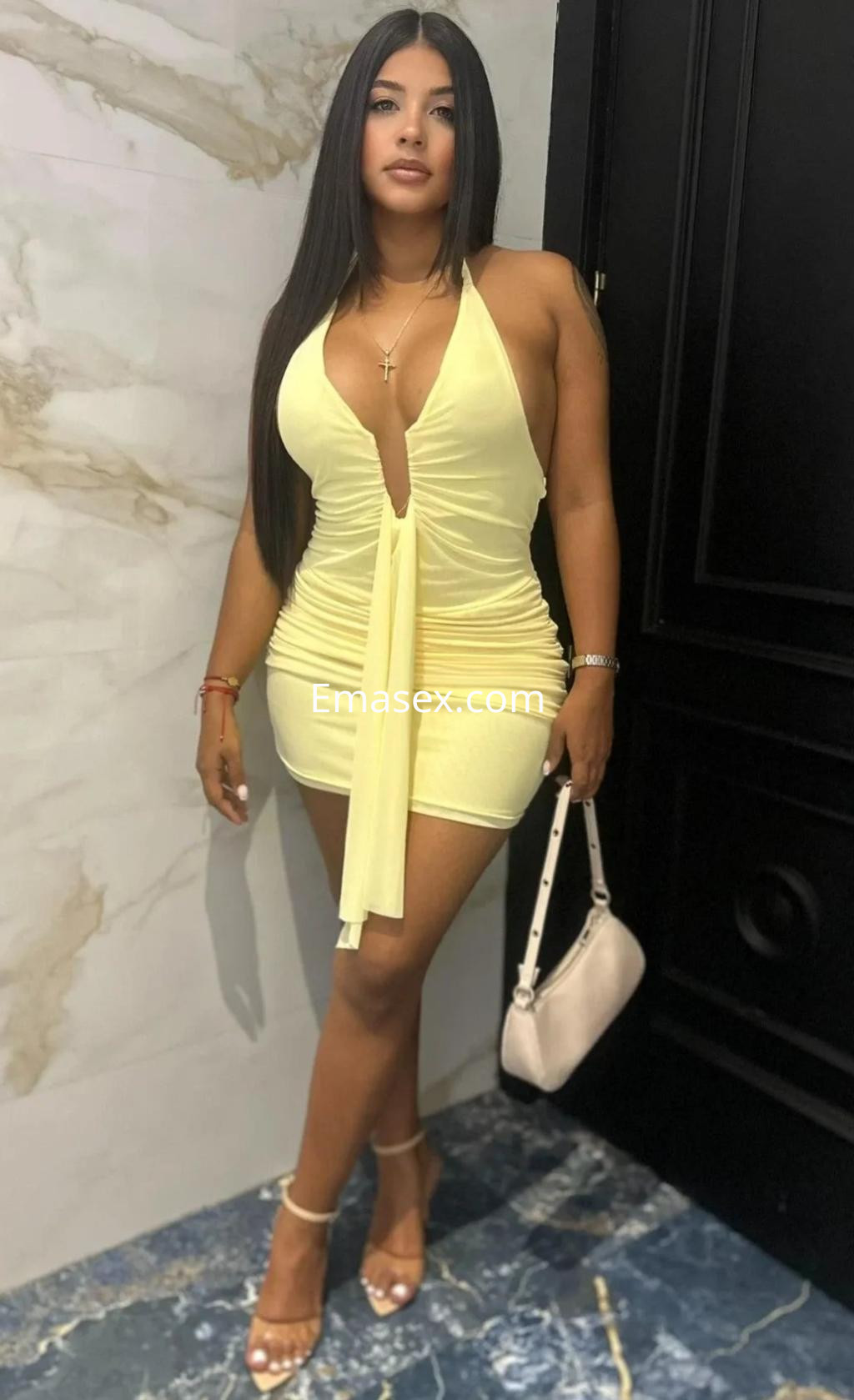Puta en Málaga viste un ajustado vestido amarillo con escote profundo y sandalias, posando con una bolsa.