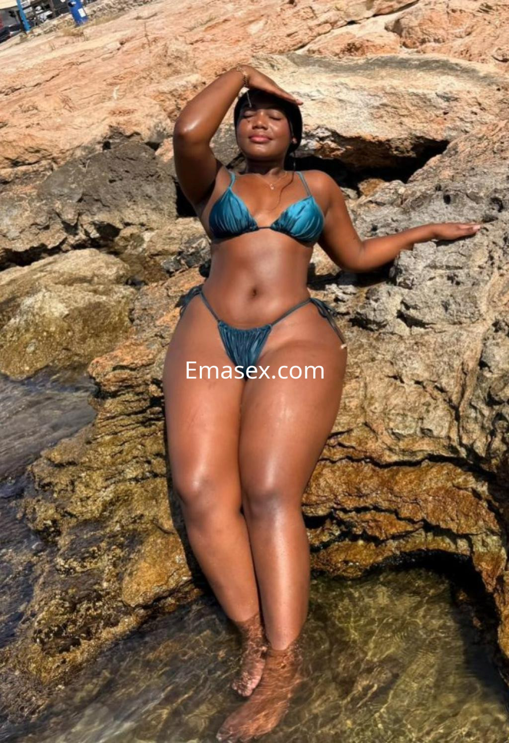 La puta posa en una playa de Alicante, luciendo un bikini azul y disfrutando del sol junto a las rocas.