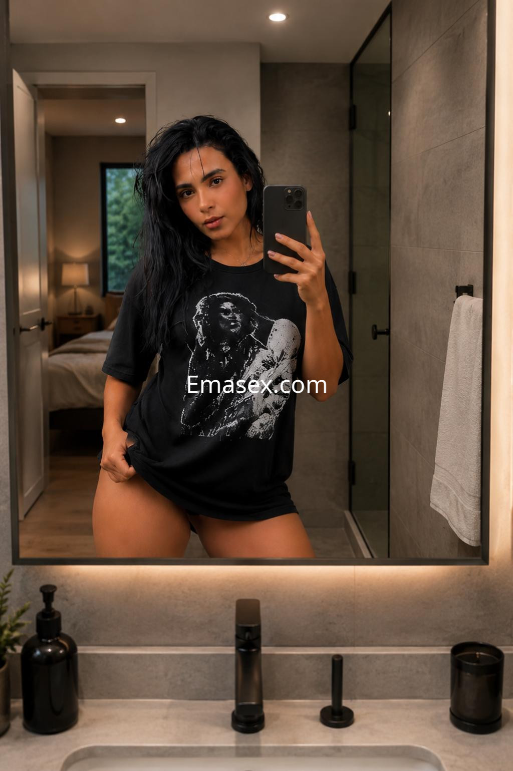 Escort en Murcia con camiseta negra amplia y shorts cortos, posando frente al espejo en un baño moderno.