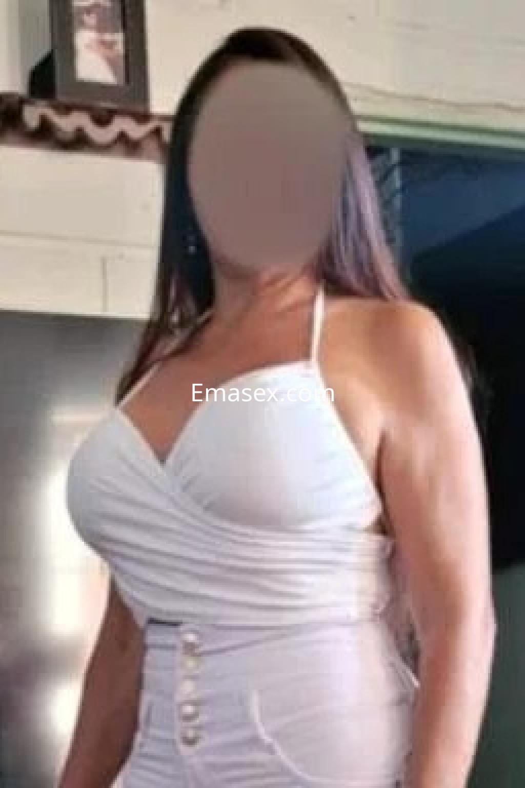 Puta de Cádiz con vestido blanco ajustado, mostrando sus curvas y cabello largo, posando en un interior luminoso.