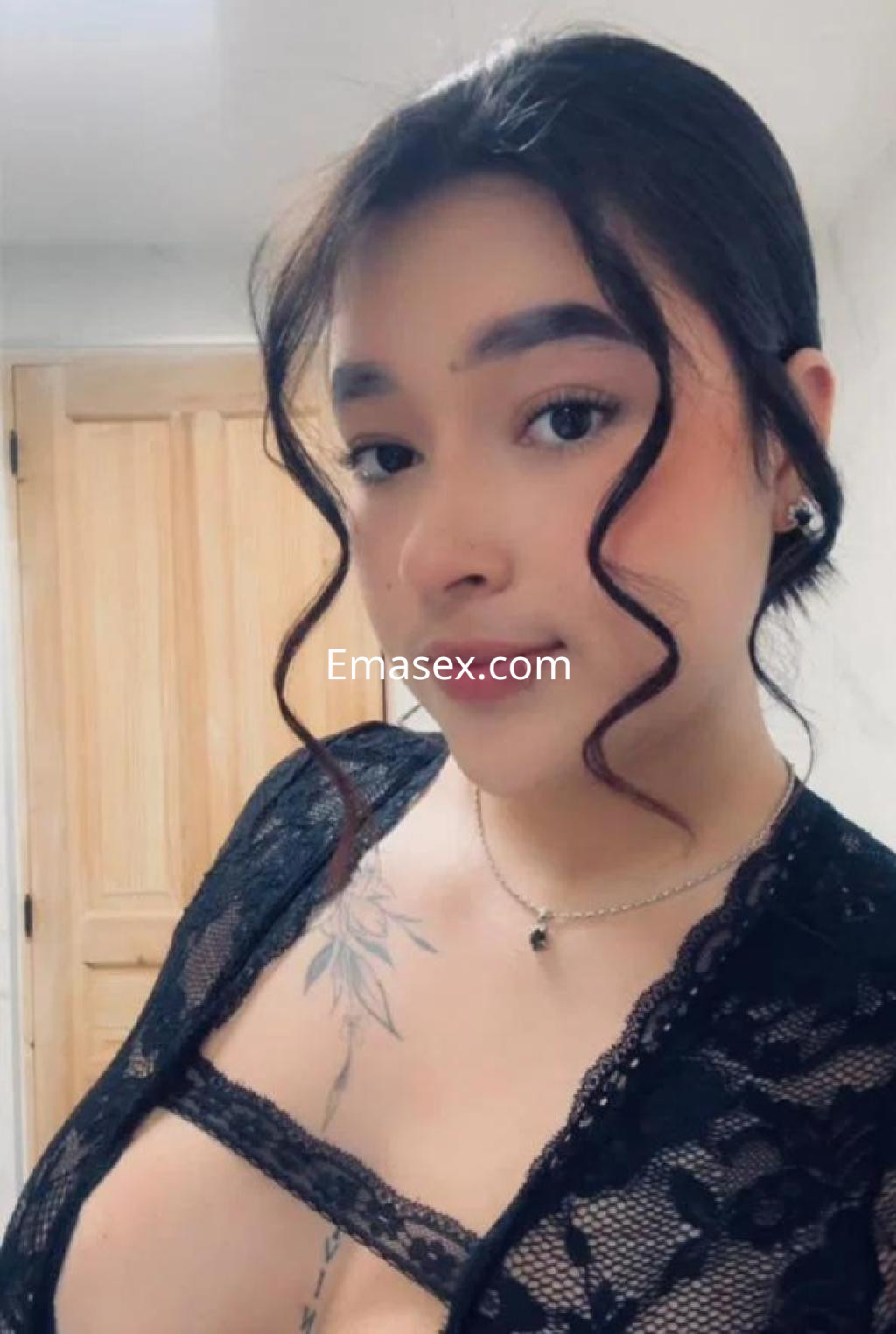 Escort en Castellón con cabello oscuro y rizado, vistiendo una blusa de encaje negro y mostrando un tatuaje en el pecho.