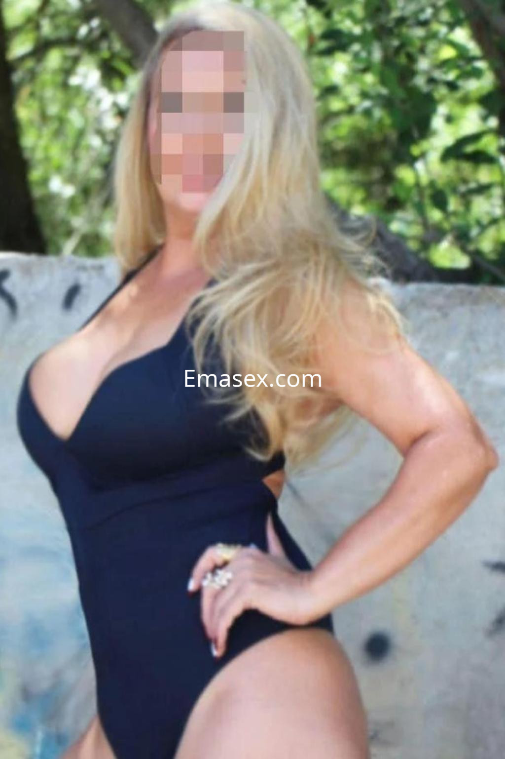 Escort en Salamanca posando con un traje de baño negro, luciendo cabello largo y rubio en un entorno natural.