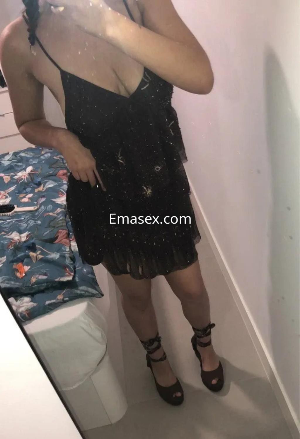 Puta en Córdoba con un vestido negro corto y detalles brillantes, posando frente a un espejo.