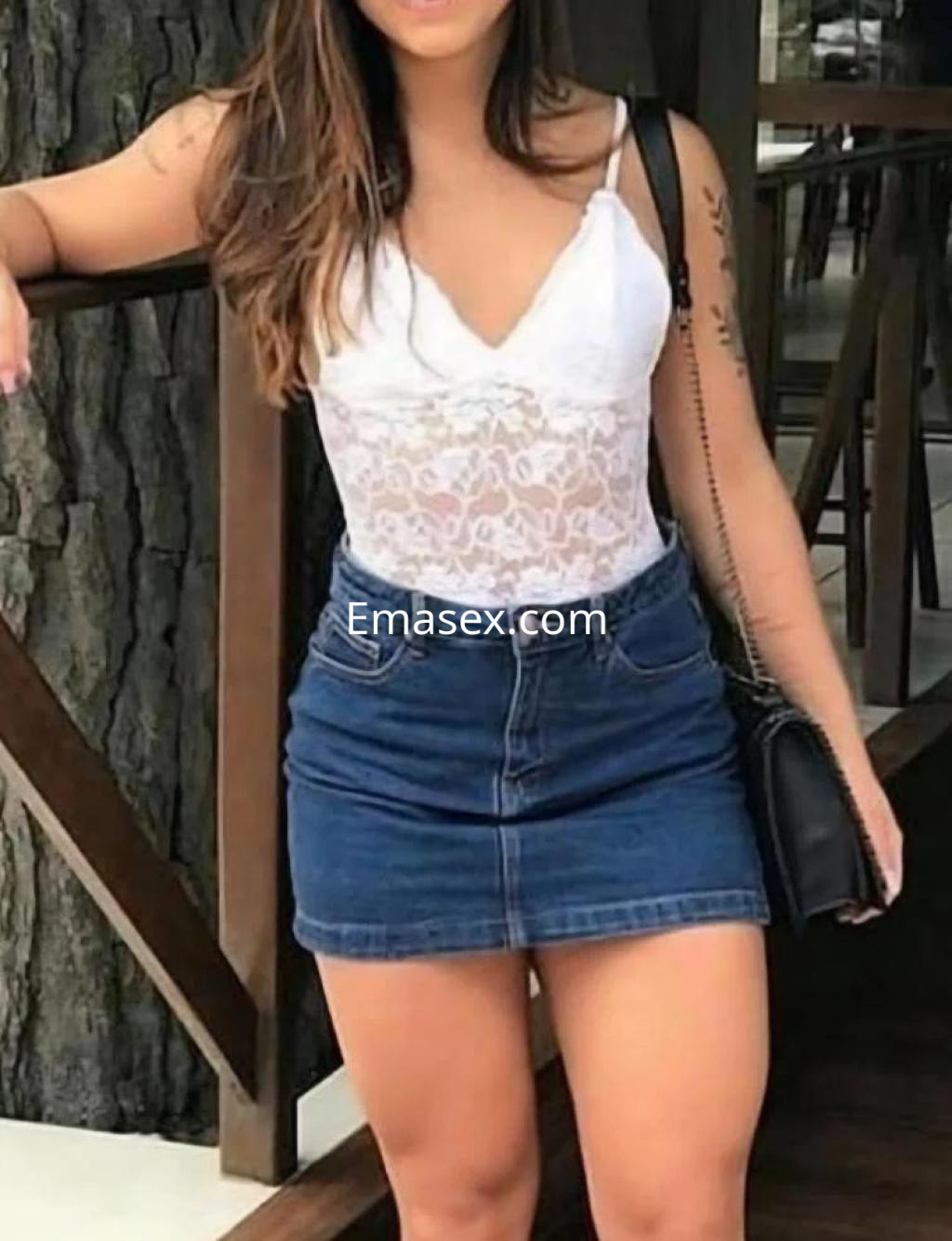 Escort en León con blusa blanca de encaje y falda de mezclilla, posando con una mano en la cadera.