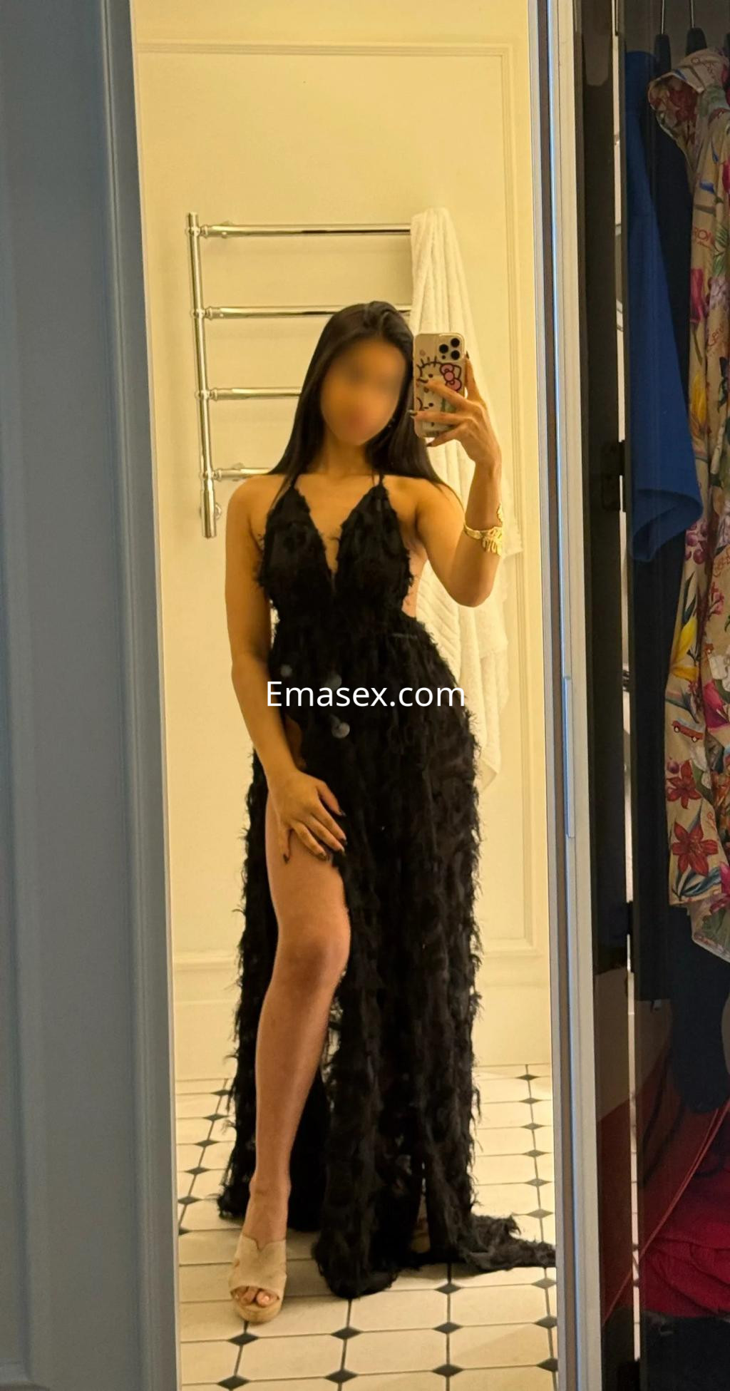 La puta luce un vestido negro largo con plumas y una abertura lateral, en un entorno de baño en Valencia.