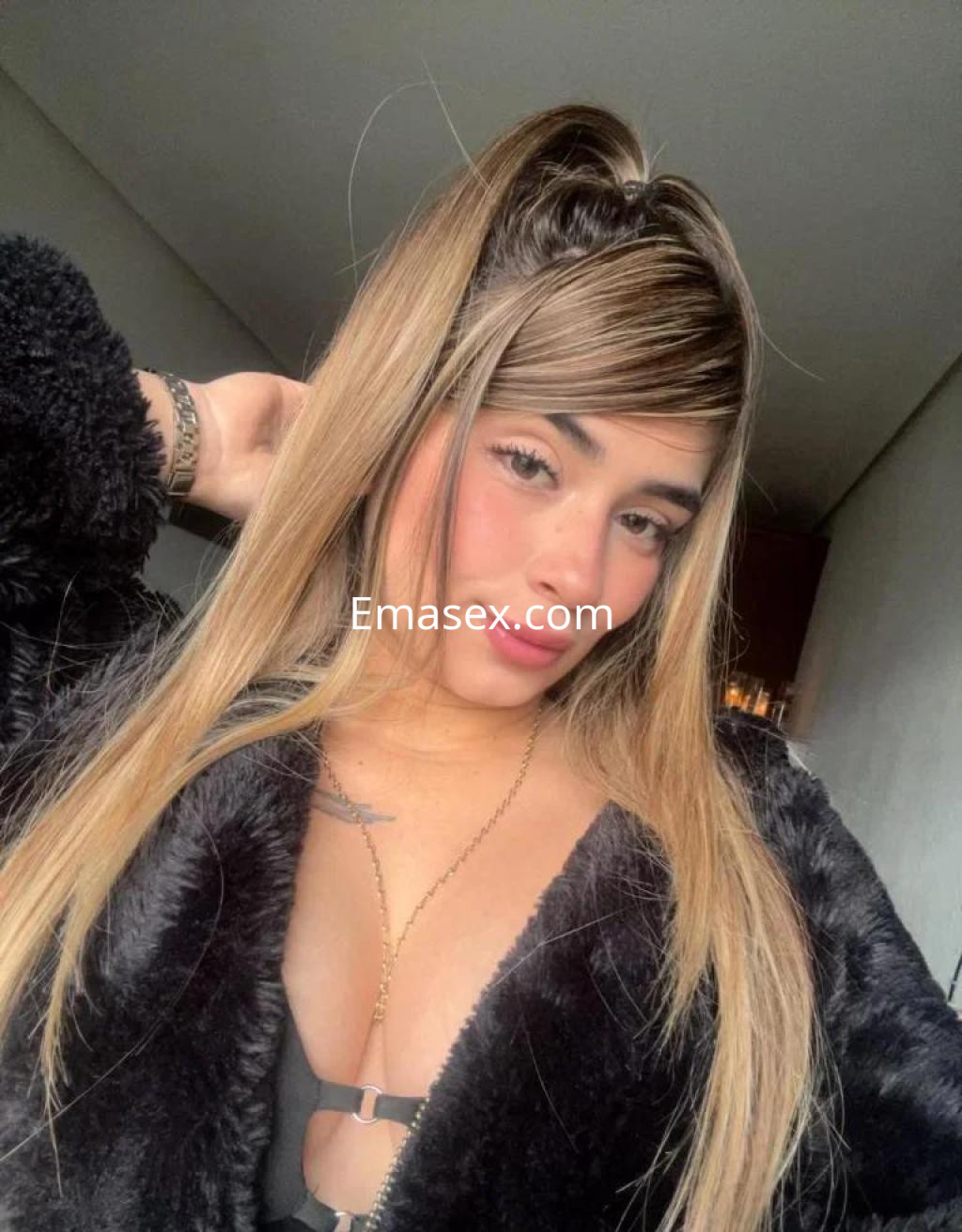 Escort en Zaragoza con cabello largo y lacio, usando un abrigo de piel negra y posando suavemente.
