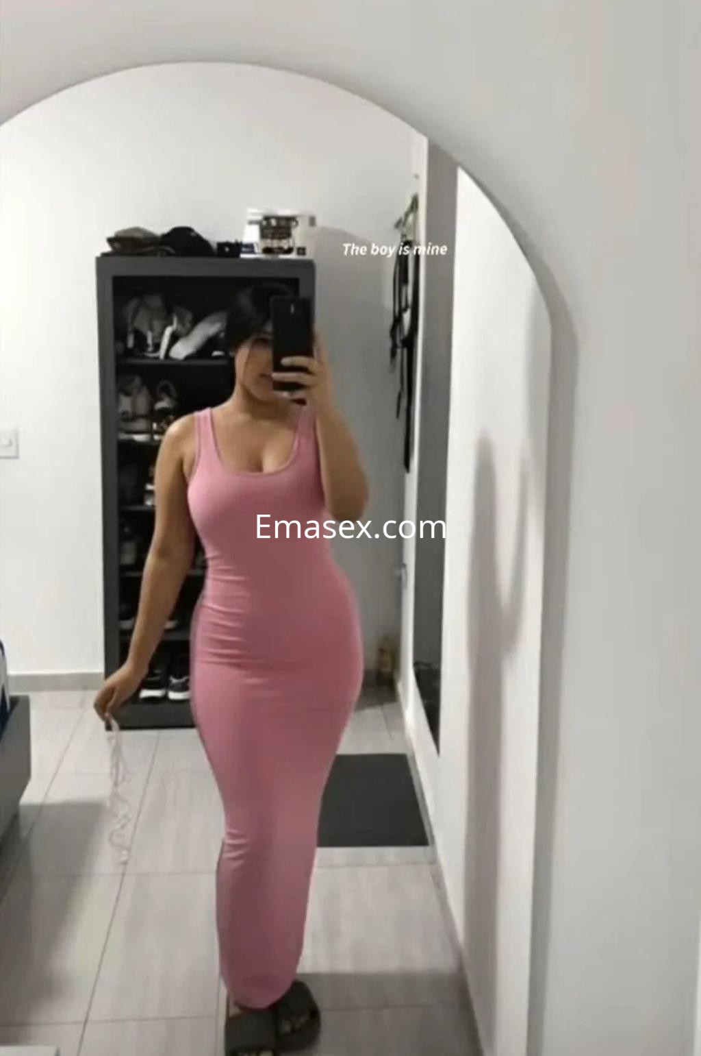 La puta posa en un vestido ajustado de color rosa, frente a un espejo en un ambiente minimalista en Gijón.