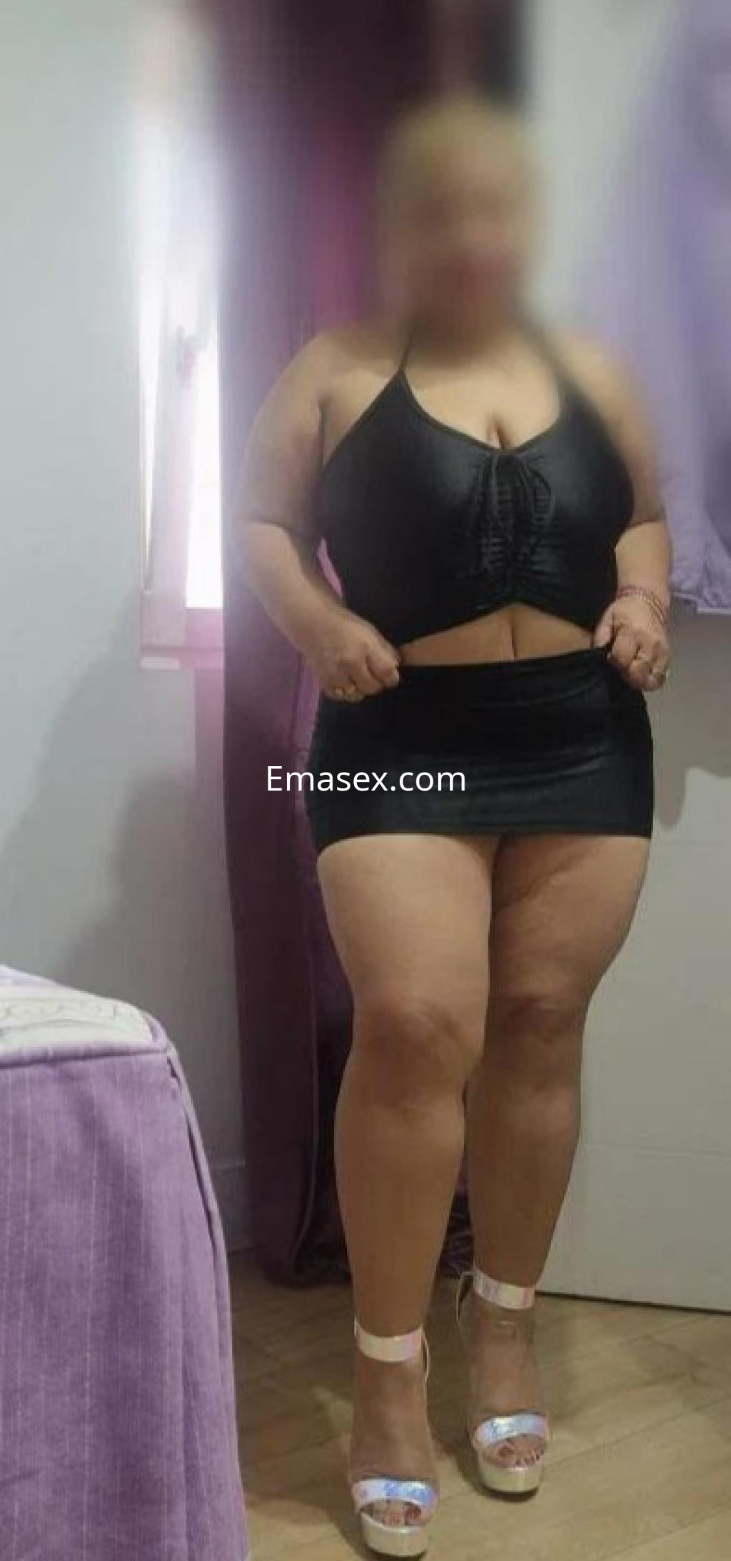 Puta en Madrid, luciendo un top negro y una falda corta, con sandalias altas en un entorno interior.