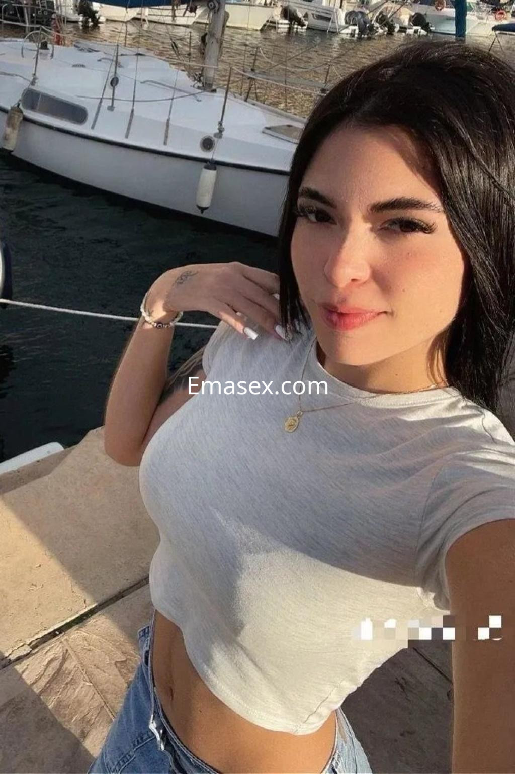 Puta en Málaga luce una camiseta ajustada y jeans, posando con una mano en el puerto deportivo.