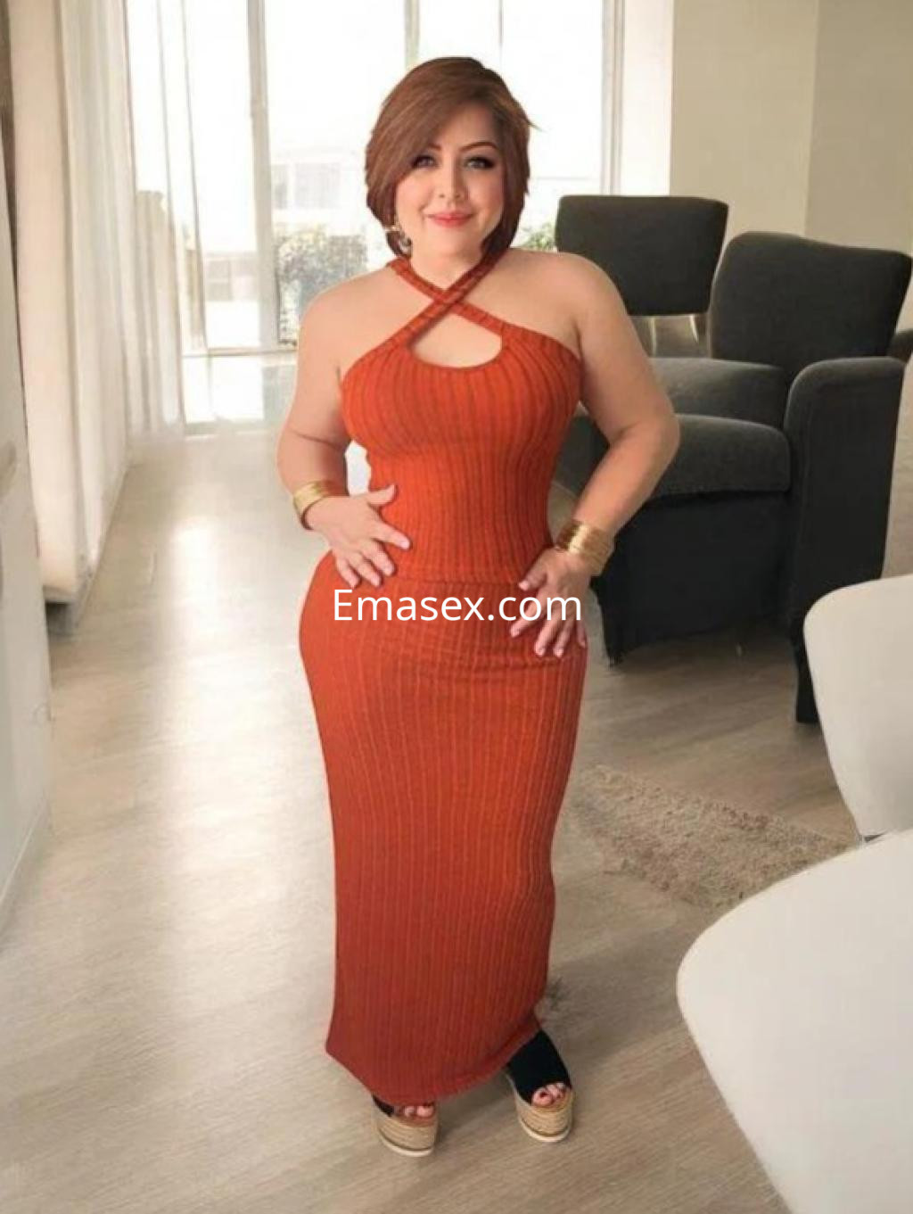 Escort en Logroño luciendo un vestido largo de tirantes en tono naranja y sandalias de plataforma, posando en un ambiente luminoso.